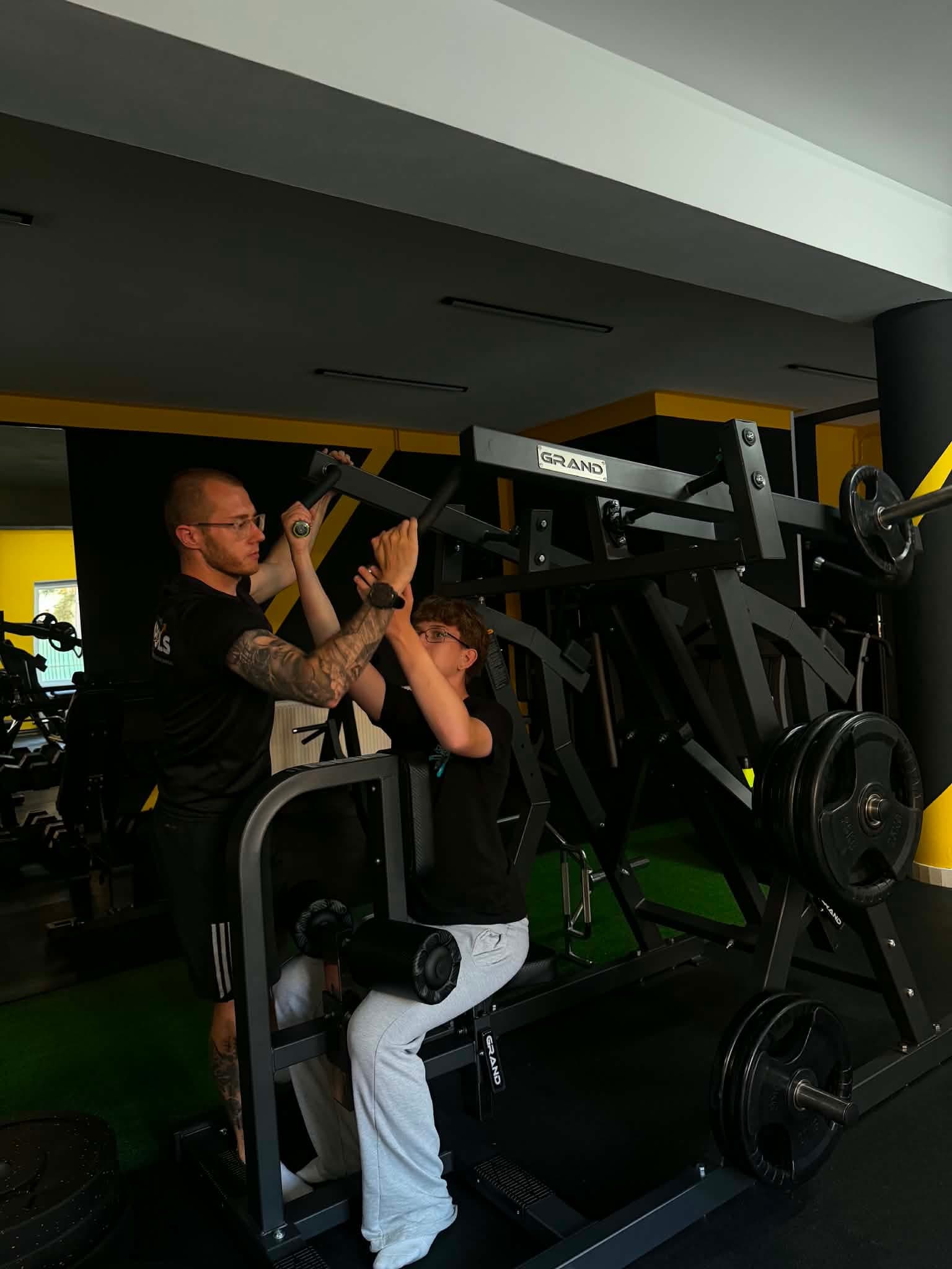 Trener koryguje technikę wyciskania mężczyzny na maszynie w studio Tylko Impuls.